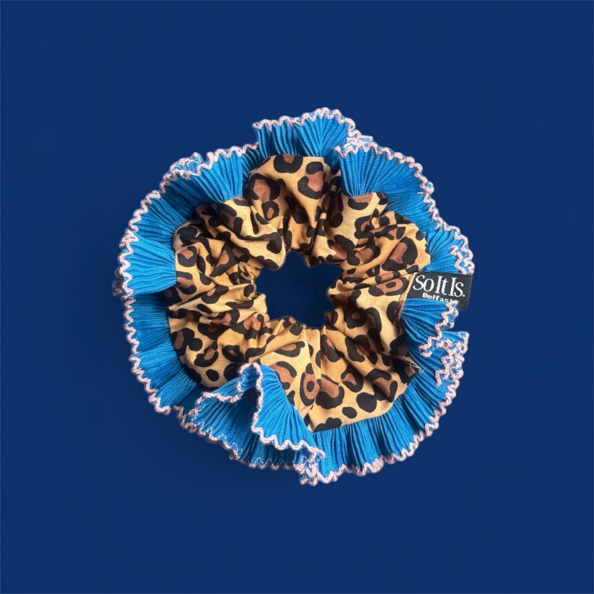 Leopard print scrunchie with blue ruffled edge on a navy background