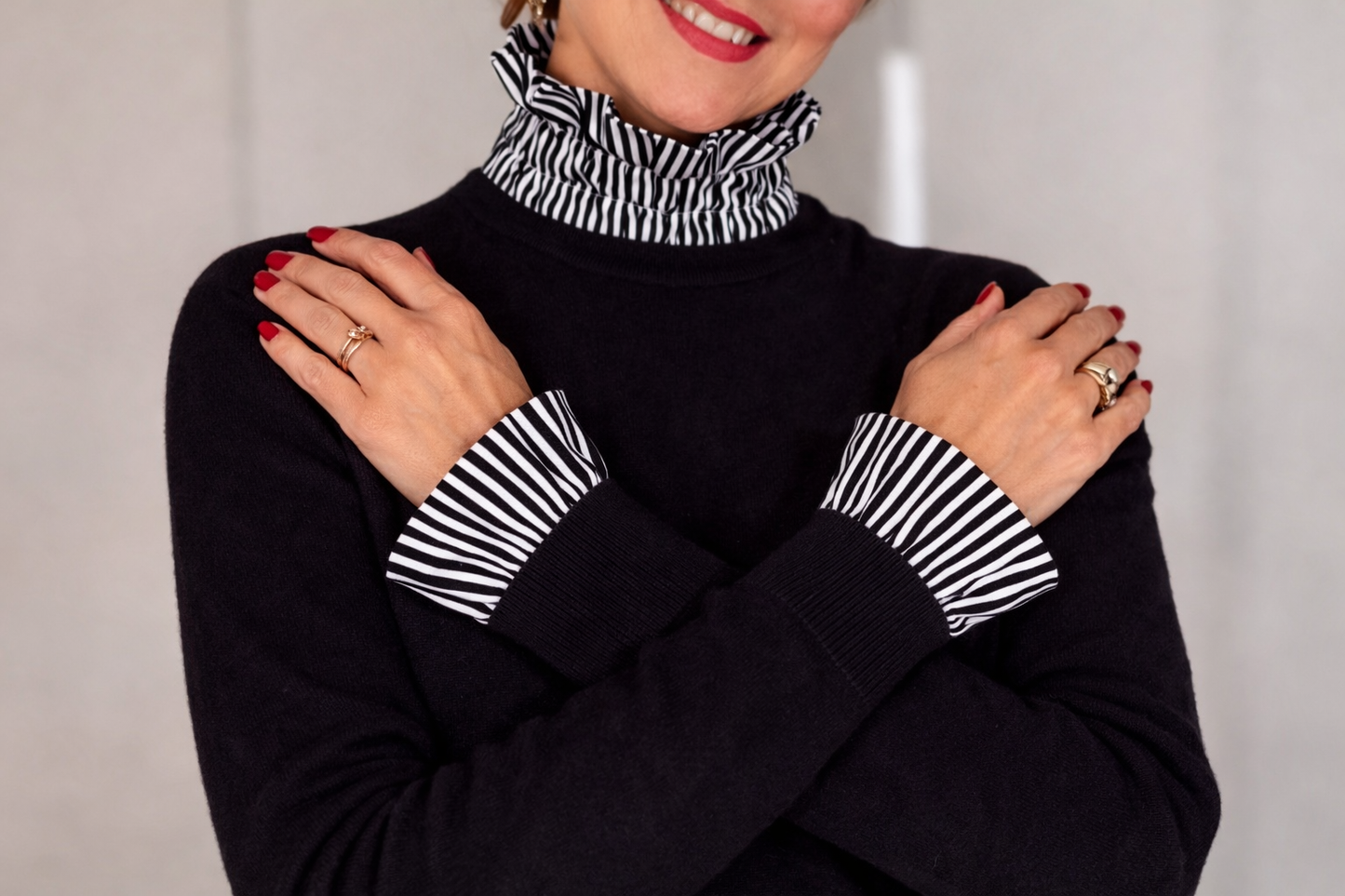 Black sweater layered with a black and white striped ruffle high neck and matching cuffs, styled on model with crossed arms