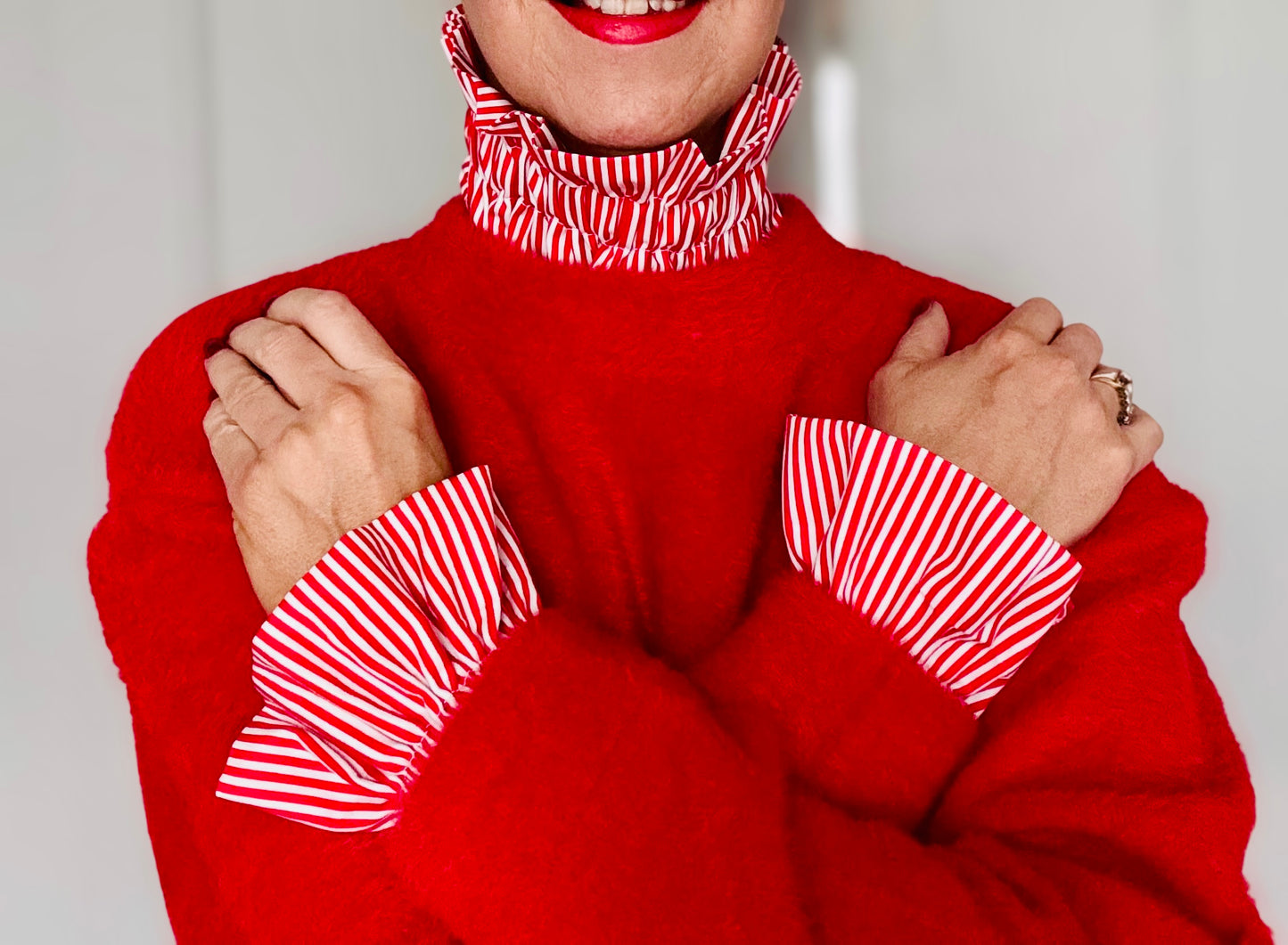 Red knit jumper layered over a red and white striped blouse with statement ruffle collar and oversized ruffle cuffs, close-up styling detail.