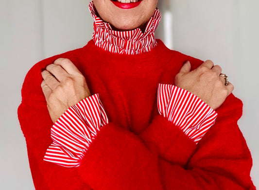 Red knit jumper layered over a red and white striped blouse with statement ruffle collar and oversized ruffle cuffs, close-up styling detail.